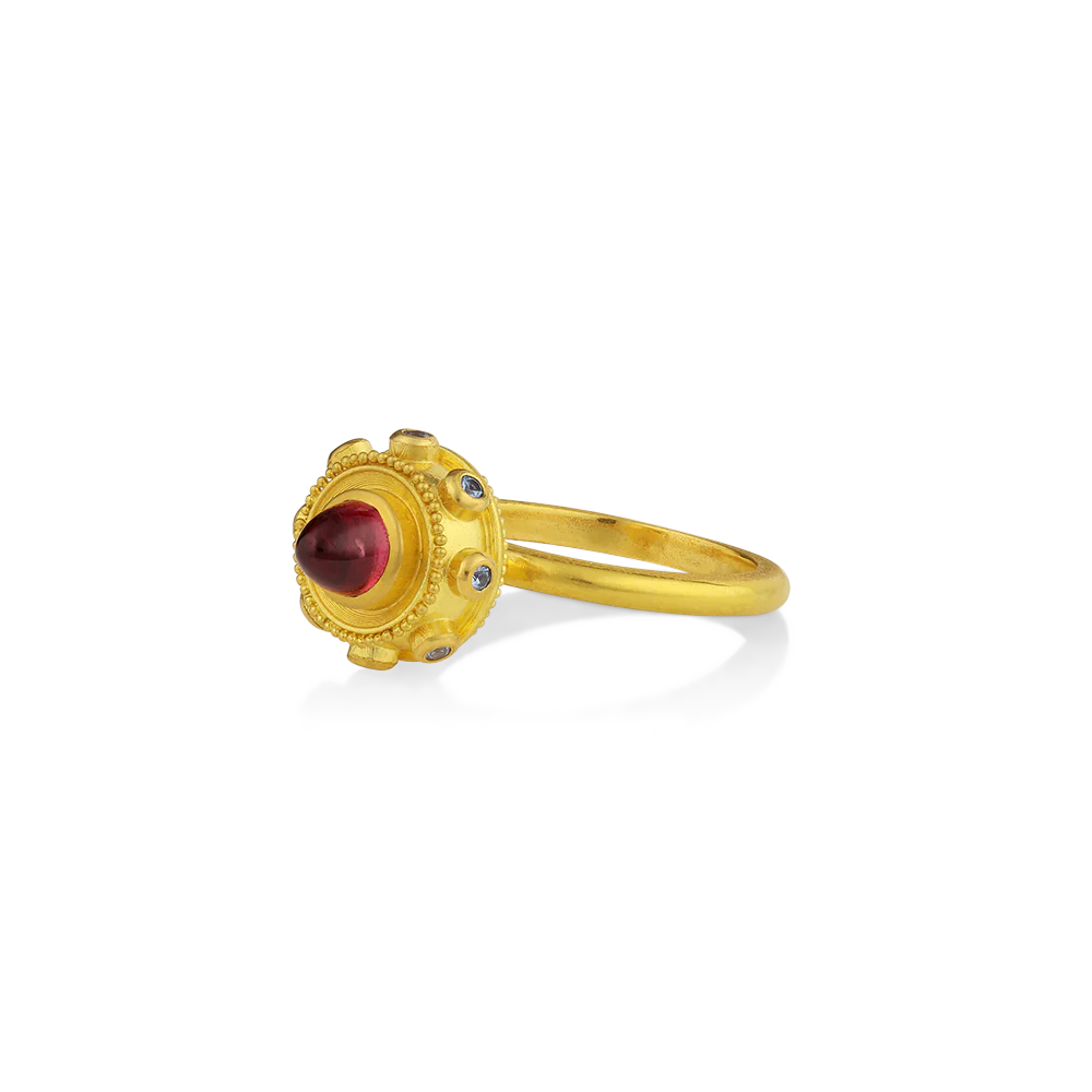 Reminiscent of a bejeweled Orb, instead of a customary cross mounted top it, this one has a purplish red rhodolite garnet cut in a bullet style cabochon. A band of periwinkle blue Yogo sapphires from Montana and golden balls of granulation float around it like tiny moons.

Made in recycled 22k yellow gold, Mozambique rhodolite garnet (1.19ctw) and Montana sapphires (.16ctw). Size 7. Can be resized.