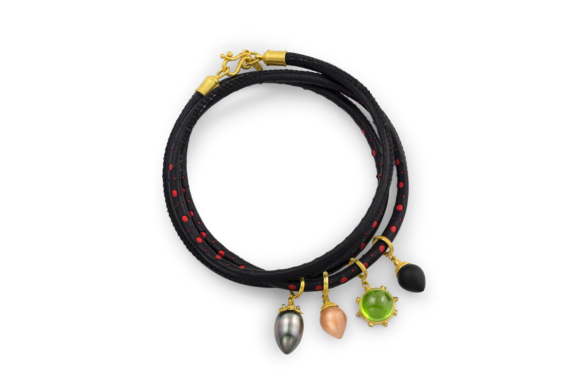Pointed drop Tahitian pearl charm shown on a red and black spotted leather bracelet with other charms.