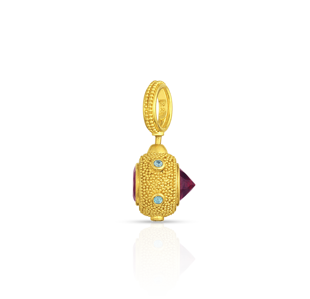 Deep purplish red rhodolite garnets set in reverse at the front like a spike, regular set at the back give a medieval look to this distinctive charm. A distinct and different choice for everyday wear. Bright blue zircon studs set around the hexagons provide a discreet sparkle and pop of color. Length approximately 35 mm or 1.38 in. Made from recycled 22k yellow gold, rhodolite garnets (2.15ctw) and blue zircons (.11ctw).