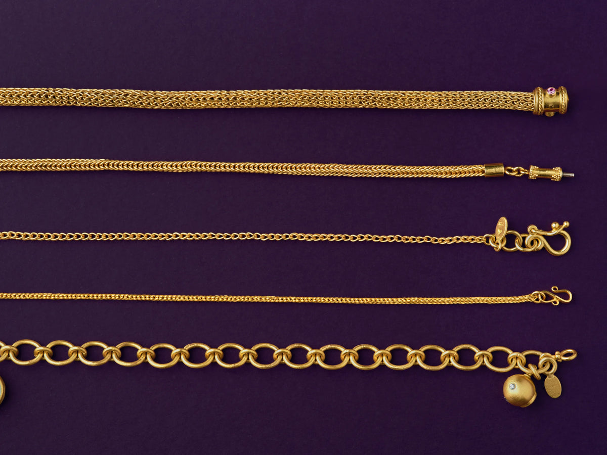 Five handmade 22k gold chains in different weaves — Viking knit, foxtail, curb, wheat, and cable link — with granulated and gemstone-set clasps