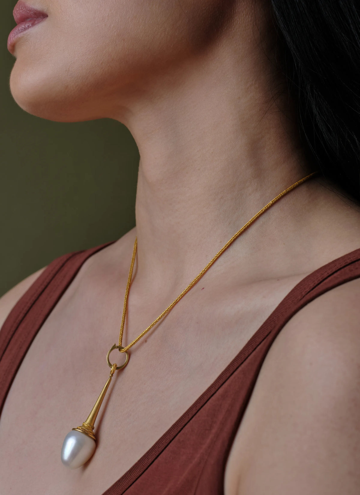 A woman wearing a 22k gold chain necklace with a baroque pearl drop pendant