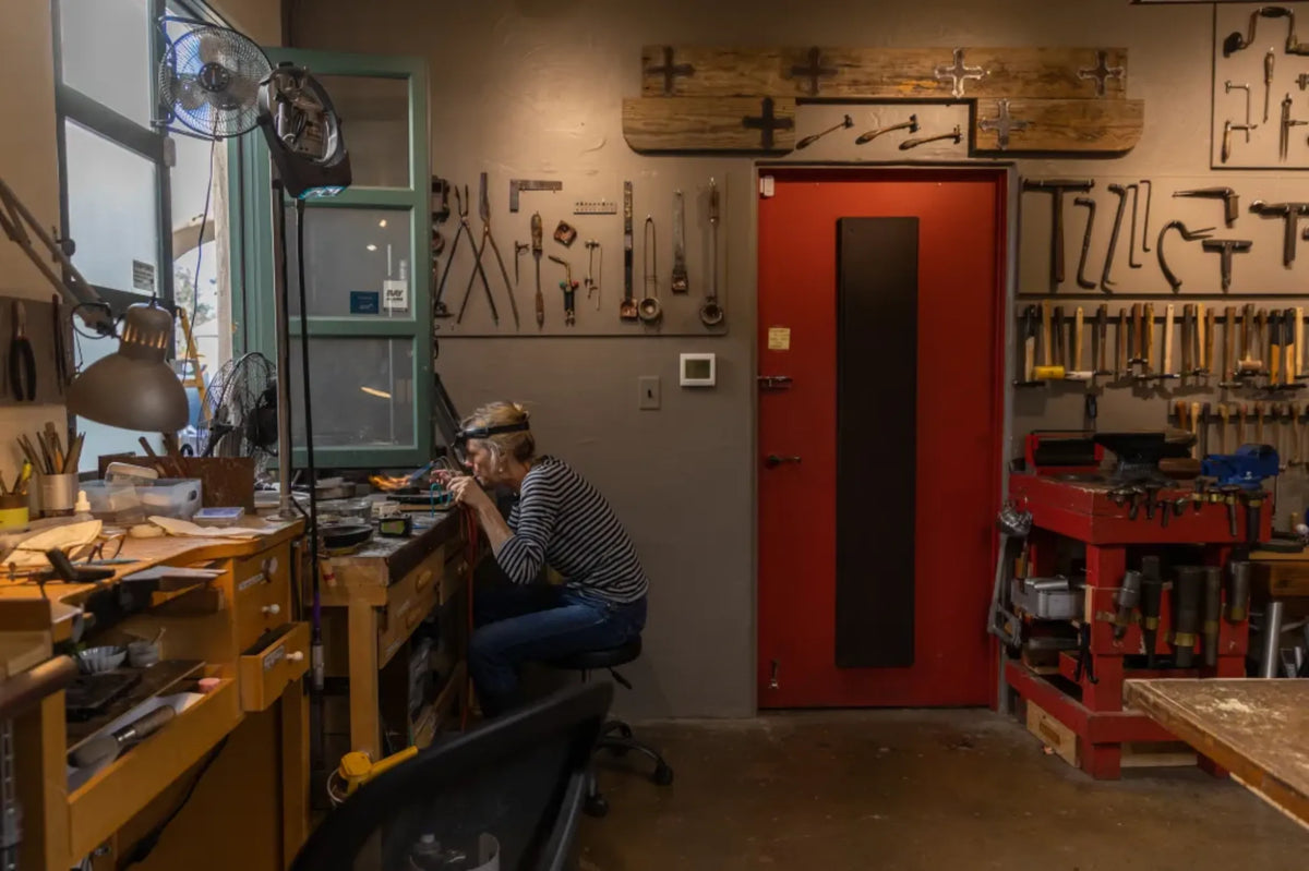 Sharona Wolff at her workbench soldering, surrounded by hand tools mounted on the workshop wall