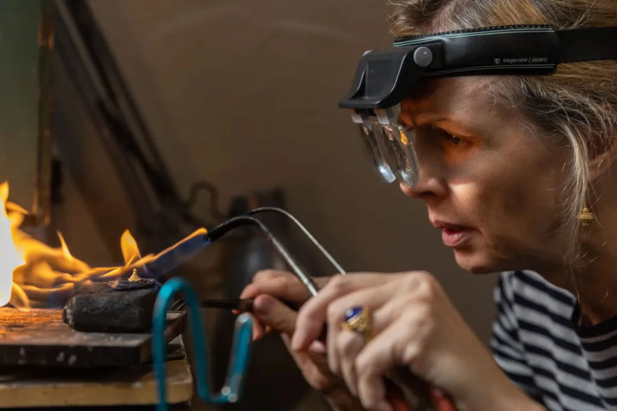 Sharona Wolff hand-soldering a gold piece at the torch, wearing a jeweler's loupe, in the Atelier Wolff workshop