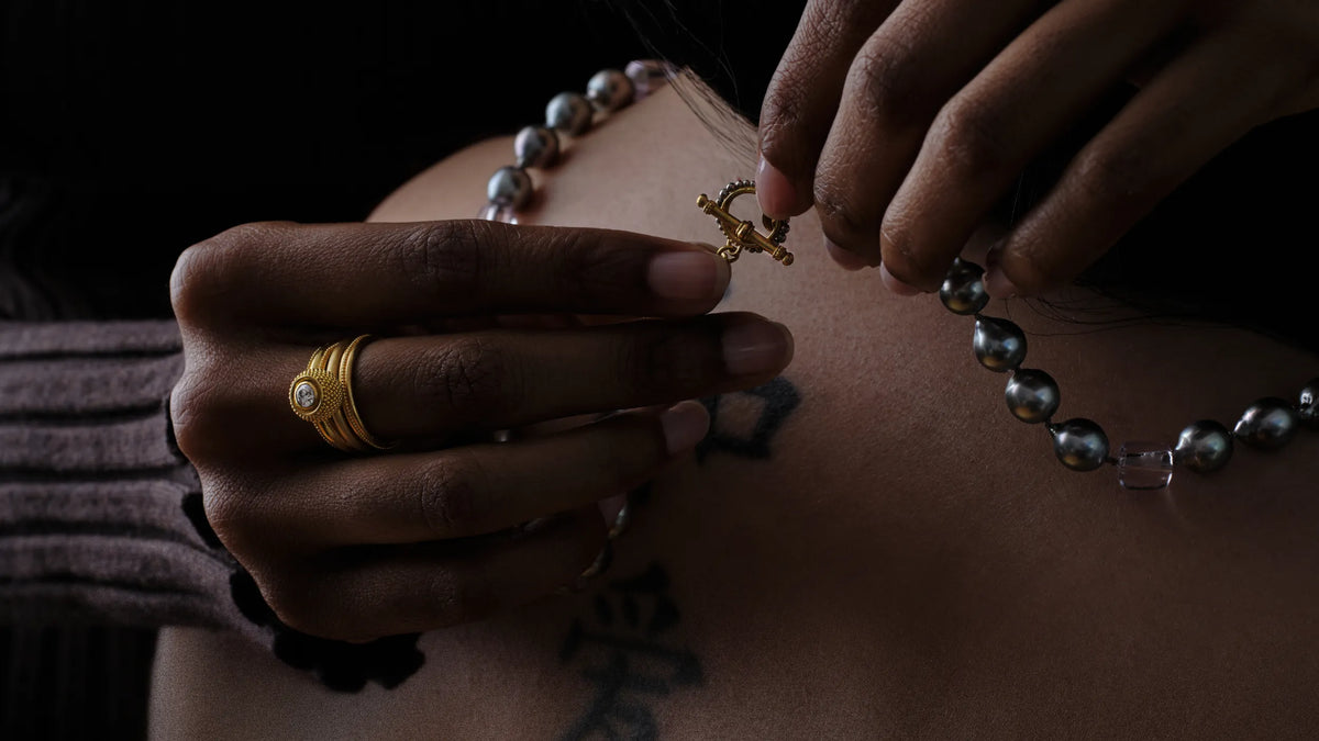 Close-up of hands fastening a granulated gold toggle clasp on a Tahitian pearl necklace
