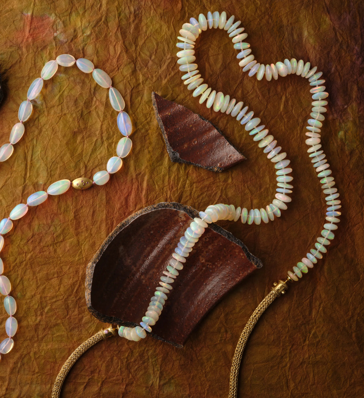 Two strands of opal bead necklaces with 22k gold granulated clasps draped across broken terracotta pottery shards