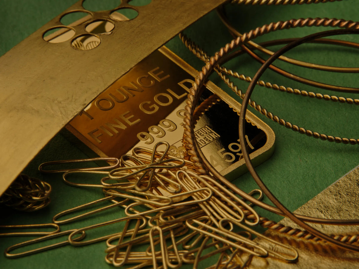 A one ounce fine gold bar alongside coiled gold wire, chains, and paperclips, representing recycled gold used in Atelier Wolff jewelry