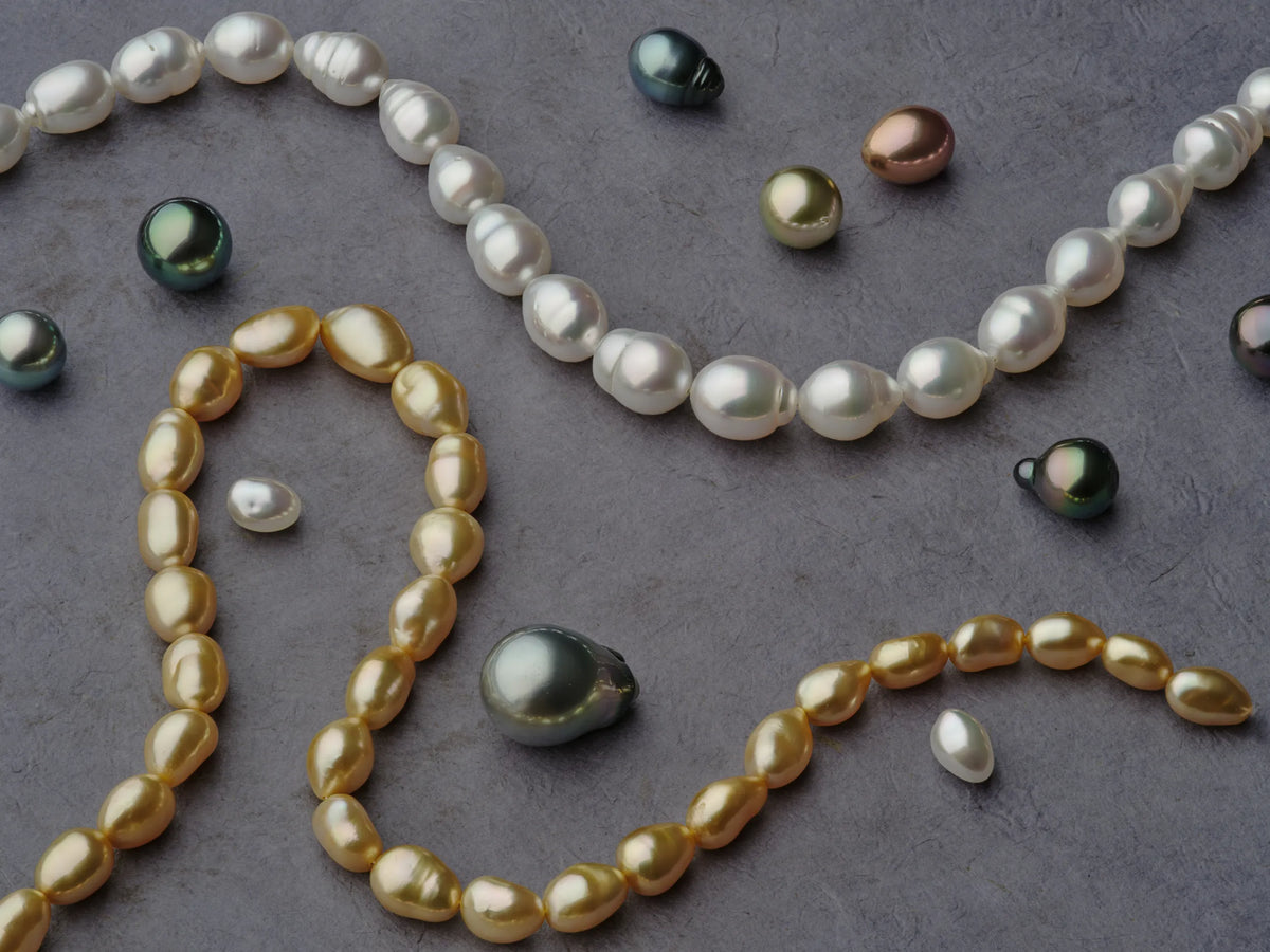 Loose white, golden South Sea, and Tahitian pearls of varying colors and sizes on a grey background