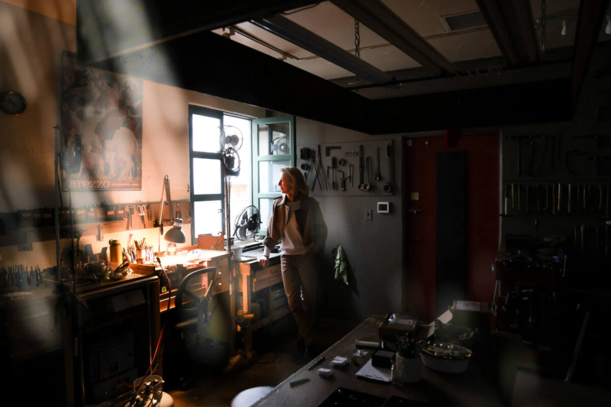 Sharona Wolff standing at the window of her goldsmithing workshop, surrounded by hand tools and jeweler's equipment
